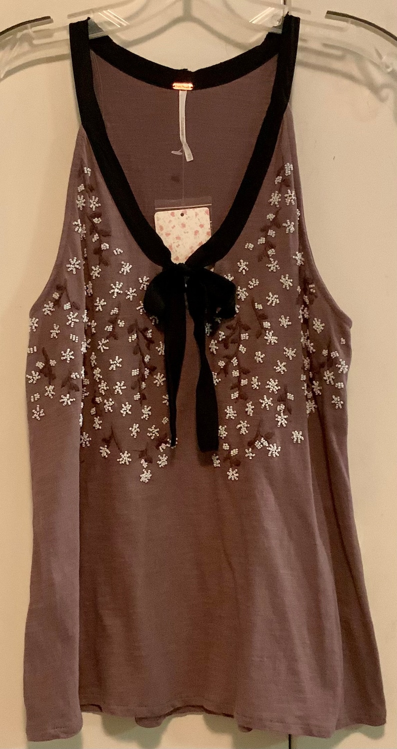 May include: A brown sleeveless top with a black bow and white floral embroidery. The top has a black trim around the neckline.