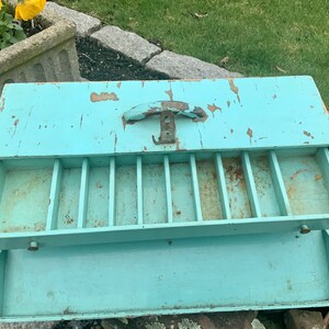 May include: A vintage, light blue wooden box with a hinged lid and a metal handle. The box has multiple compartments inside and is in a distressed condition.