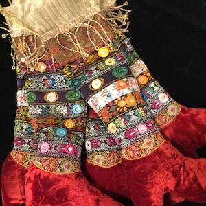 May include: A colorful, multi-layered fabric skirt with red velvet trim and a gold beaded top. The skirt is decorated with embroidered flowers, sequins, and mirrors.