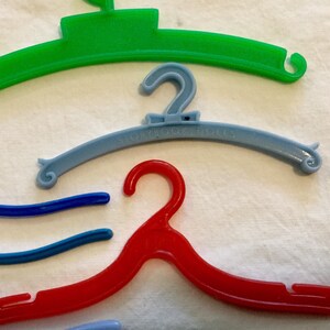 May include: A set of four plastic hangers in different colors: green, blue, light blue, and red. The light blue hanger has the text "Storybook Dolls" printed on it.