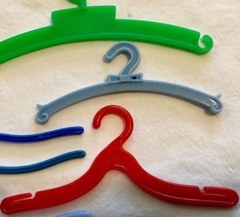 May include: A set of four plastic hangers in different colors: green, blue, light blue, and red. The light blue hanger has the text "Storybook Dolls" printed on it.