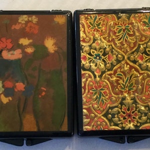 May include: Two small, rectangular boxes with black frames. One features a floral still life in shades of orange, yellow, and blue. The other has a gold, red, and green ornate pattern.
