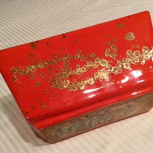 May include: A bright orange ceramic planter with a gold speckled design. The planter has a rectangular shape with rounded edges.