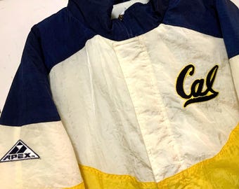 May include: A vintage jacket in navy blue, cream, and yellow. The jacket features the word "Cal" in a script font on the chest and the "APEX" logo on the sleeve. The jacket has a zip-up front and a high collar.
