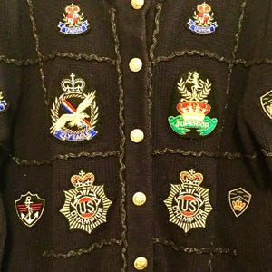 May include: A black knitted cardigan with a variety of colorful embroidered patches. The patches feature crowns, eagles, and the words "Union", "Superior", "Fly Eagle", and "US Champion".