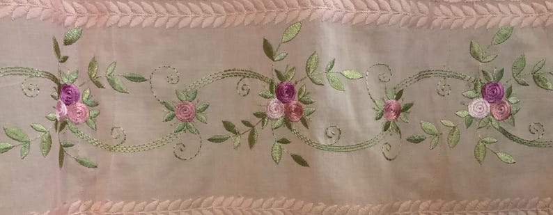 May include: Pale pink sheer fabric with embroidered floral and leaf design. The embroidery features clusters of pink and purple roses with green leaves and stems. The top and bottom edges have a decorative leaf pattern.