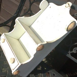 May include: White wooden wall shelf with three shelves and a drawer. The shelf is decorated with seashells.