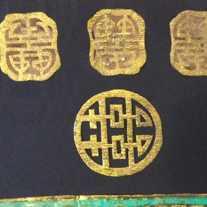May include: Four gold-colored, intricate, decorative, Chinese symbols on a black background. The symbols are in the shape of a square and a circle.