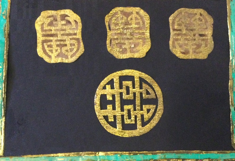 May include: Four gold-colored, intricate, decorative, Chinese symbols on a black background. The symbols are in the shape of a square and a circle.