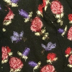 May include: Black fabric with a repeating pattern of pink, red, and purple flowers. The flowers are embroidered and have a fuzzy texture.