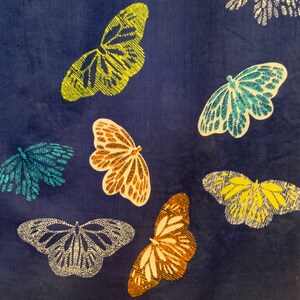 May include: A dark blue fabric with a pattern of embroidered butterflies in various colors. The butterflies are in shades of yellow, teal, orange, and white. The wings have detailed patterns.
