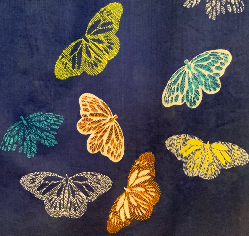 May include: A dark blue fabric with a pattern of embroidered butterflies in various colors. The butterflies are in shades of yellow, teal, orange, and white. The wings have detailed patterns.