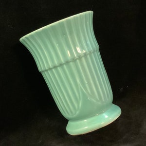 May include: A light blue ceramic vase with a fluted design. The vase has a wide mouth and a rounded base.