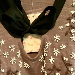 May include: A brown top with a black ribbon tie at the neck. The top is decorated with white beaded flowers and embroidered stems.
