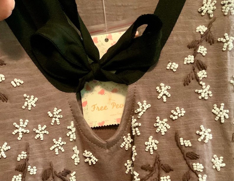 May include: A brown top with a black ribbon tie at the neck. The top is decorated with white beaded flowers and embroidered stems.