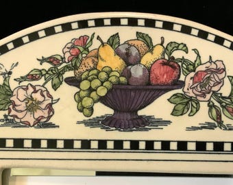 May include: A white ceramic plate with a black and white checkered border. The center of the plate features a hand-painted design of a fruit bowl filled with pears, plums, grapes, and an apple. The bowl is surrounded by roses and leaves.