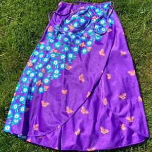 Op de afbeelding: Een paarse wikkelrok met een bloemen- en vlinderprint. De rok heeft een strik sluiting aan de taille.