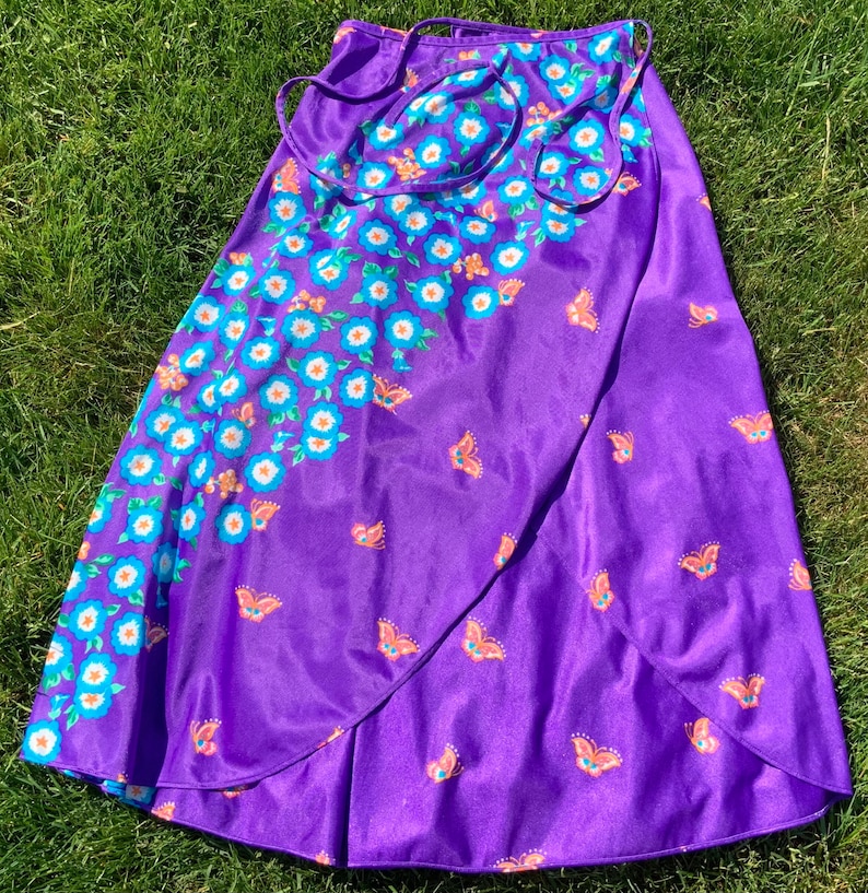 Op de afbeelding: Een paarse wikkelrok met een bloemen- en vlinderprint. De rok heeft een strik sluiting aan de taille.