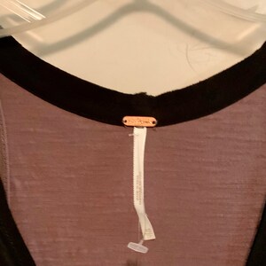 May include: A mauve sleeveless top with a black trim around the neckline and armholes. The top has a Free People tag attached to the back.
