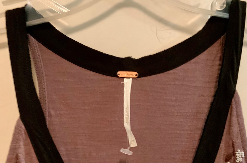 May include: A mauve sleeveless top with a black trim around the neckline and armholes. The top has a Free People tag attached to the back.
