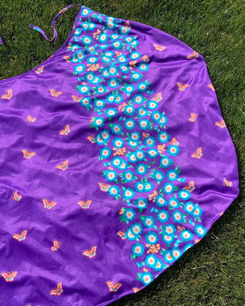 Op de afbeelding: Paarse stoffen rok met een bloemen- en vlinderprint. De rok heeft een strik in de taille en is gemaakt van een zacht, zijdeachtig materiaal.