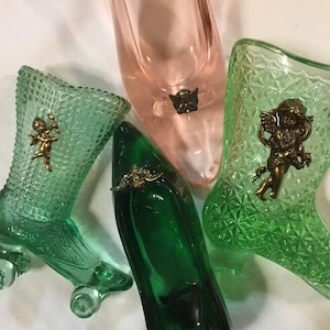 May include: Four glass slipper-shaped trinket dishes with angel cherub embellishments. Two are green, one is pink, and one is a darker green. The green dishes have a textured, diamond-like pattern.
