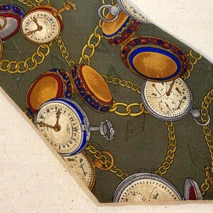 May include: Olive green necktie featuring a repeating pattern of gold pocket watches and gold chain links. The pocket watches have white faces with black numerals and hands, and are accented with red and blue details. The tie is made of a smooth fabric.