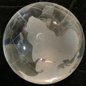 Op de afbeelding: Een heldere glazen globe met een gematteerde gegraveerde wereldkaart. De globe staat op een zwart oppervlak.