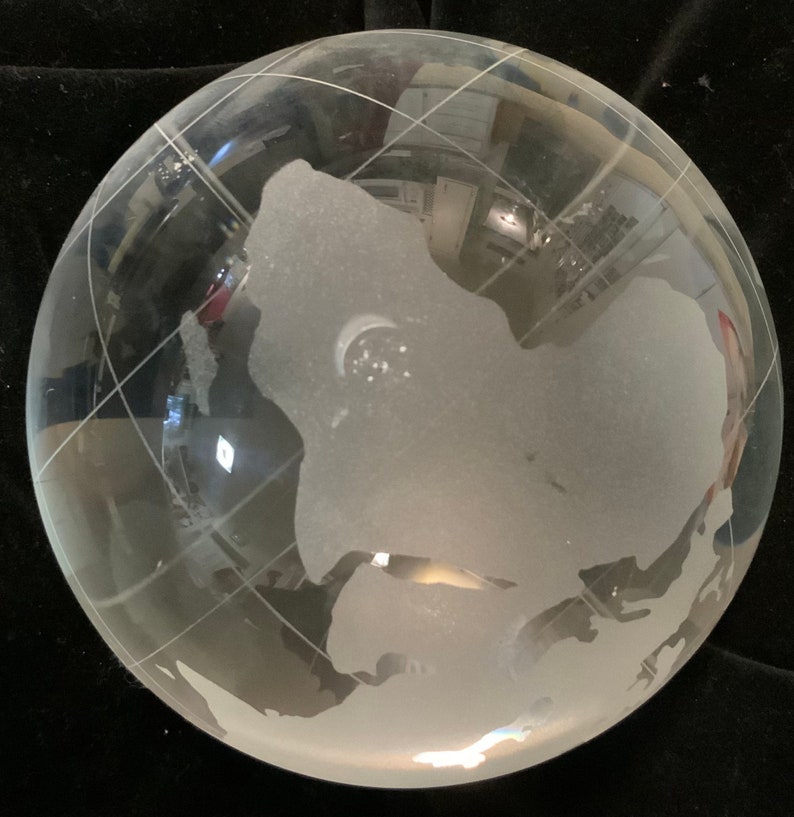 Op de afbeelding: Een heldere glazen globe met een gematteerde gegraveerde wereldkaart. De globe staat op een zwart oppervlak.