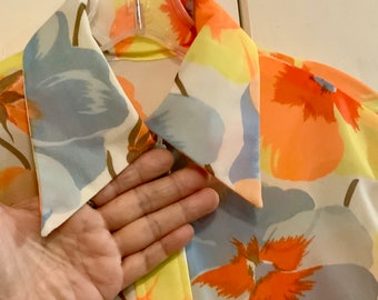 May include: A white, yellow, and orange floral print shirt with a pointed collar. The collar is folded down and the shirt is hanging on a hanger.