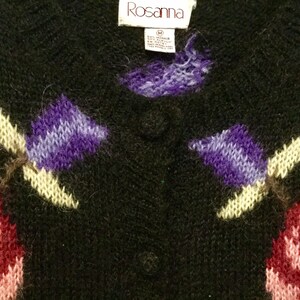 May include: Black fuzzy cardigan with a floral design. The flowers are pink, red, purple, and yellow. The cardigan has a button closure and the label "Rosanna" is visible.