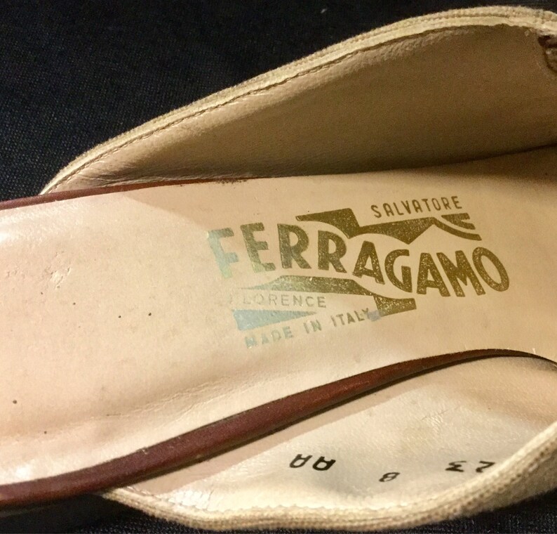May include: Close-up of the inside of a beige shoe with a brown leather trim. The shoe is labelled "Salvatore Ferragamo Florence Made in Italy" in gold lettering.