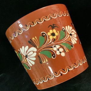 May include: A terracotta flower pot with a brown glaze and hand-painted floral designs in white, yellow, and green.