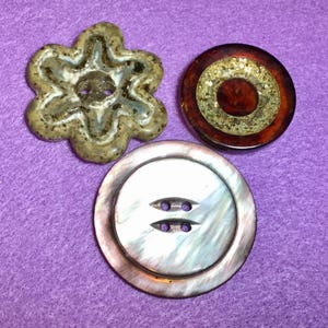May include: Three decorative buttons, one brown with a flower design, one brown with gold glitter, and one iridescent with a mother-of-pearl finish.
