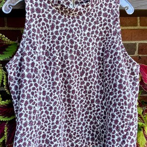 Puede incluir: Una blusa blanca sin mangas con cuello alto y estampado de leopardo marr&oacute;n.