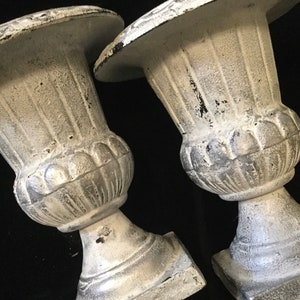 May include: Two white, decorative, cast iron urns with a distressed finish. The urns have a fluted design and a round base.