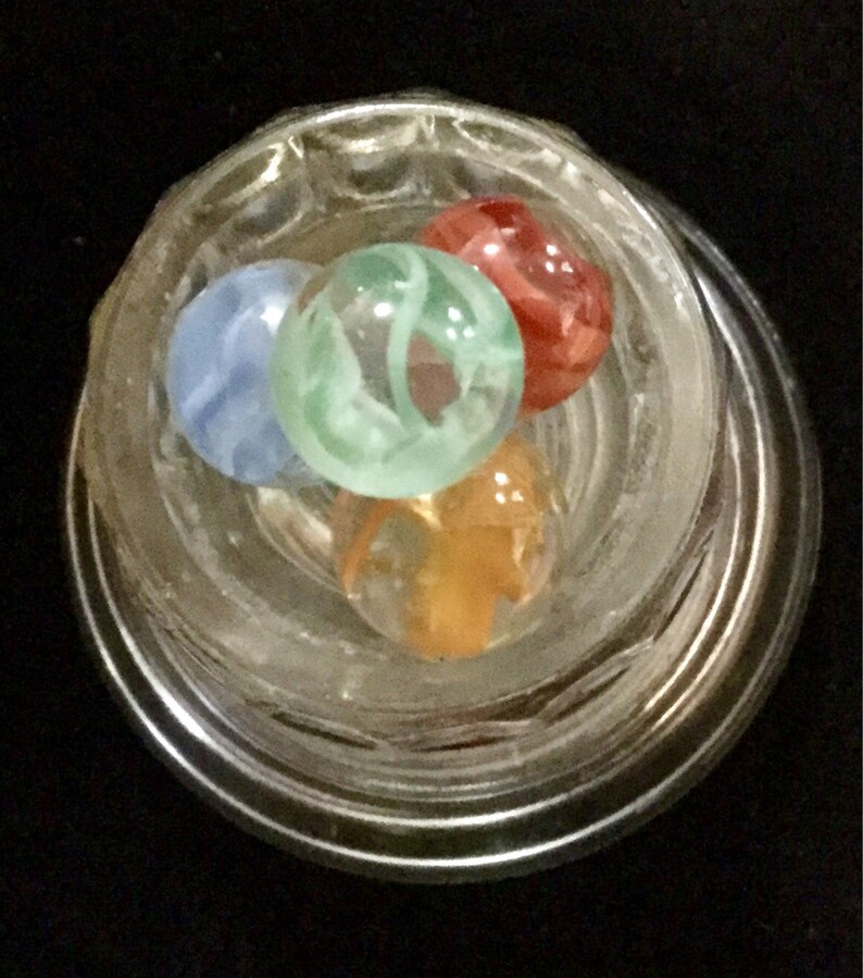 May include: Four glass marbles in a clear glass jar. The marbles are blue, green, orange, and red. The marbles have swirls of color.