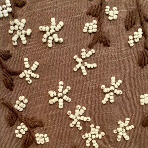 May include: Close-up of a brown fabric with white bead embroidery in the shape of flowers and branches.
