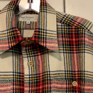 May include: A white, red, yellow, and black plaid flannel shirt with a button-down collar. The shirt has a label that reads "Paul Stuart New York" and a size "M".