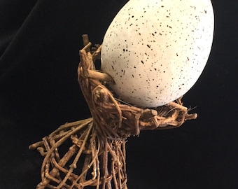 May include: A speckled white egg sits in a nest made of twigs. The nest is shaped like a pedestal.
