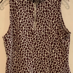 Puede incluir: Una blusa sin mangas blanca con estampado de leopardo marr&oacute;n. La blusa tiene cuello alto y una cremallera en la parte delantera.