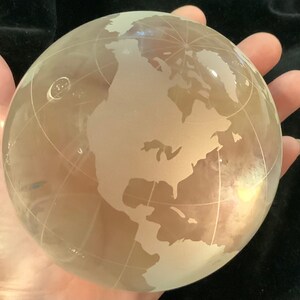Op de afbeelding: Een matglazen globe met een gedetailleerde gegraveerde wereldkaart. De globe is helder en heeft een lichte gele tint.
