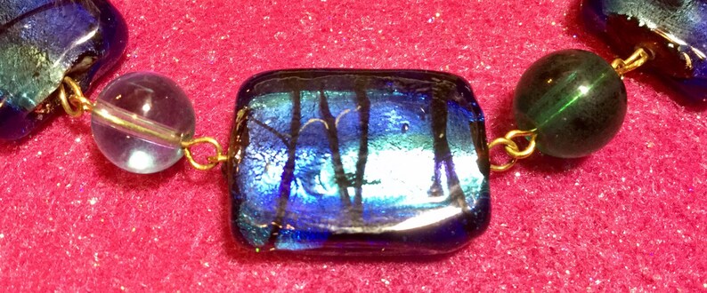 May include: A close-up of a blue and green glass bead necklace with gold accents. The beads are iridescent and have a textured surface.