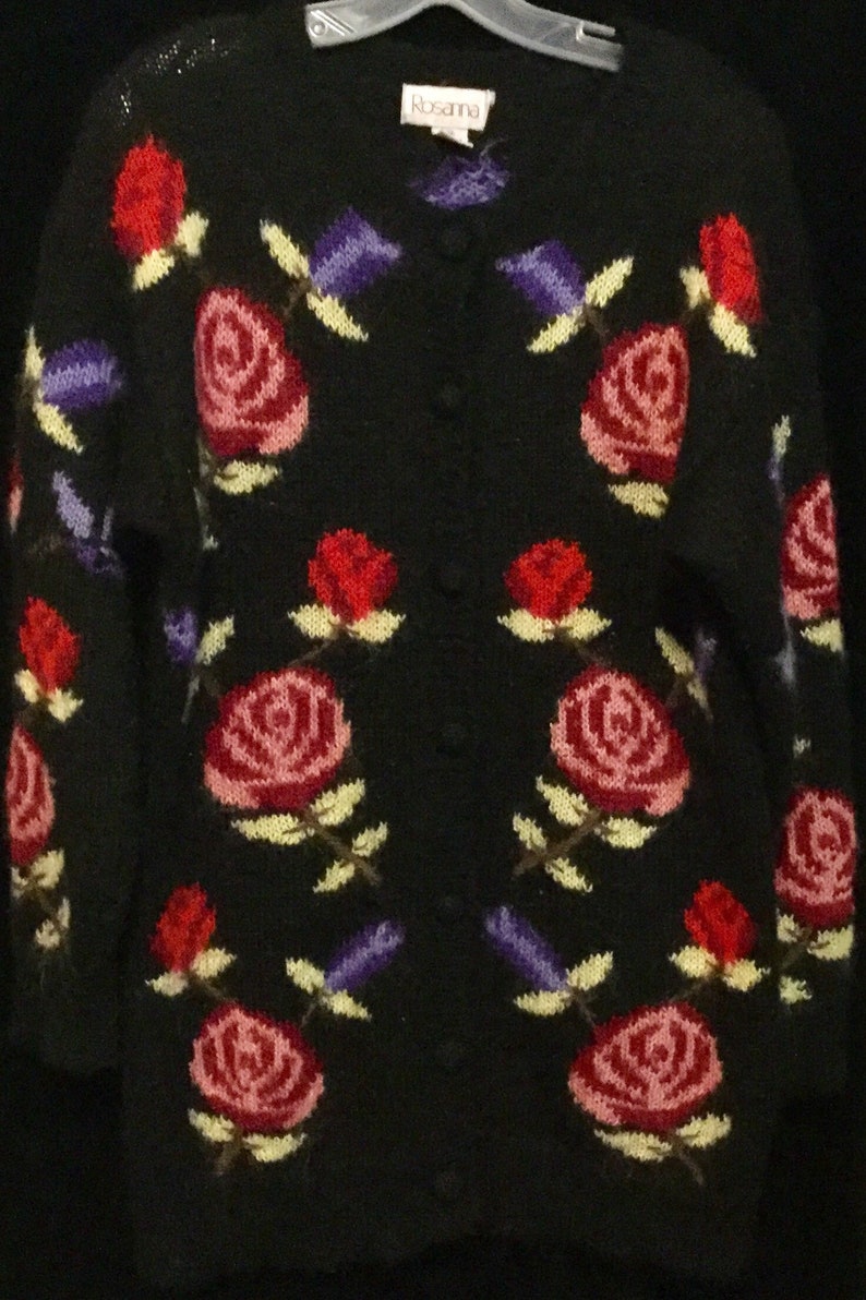 May include: Black cardigan sweater with a floral pattern of pink, red, and purple roses. The sweater has a button closure and the label "Rosanna" is visible on the front.