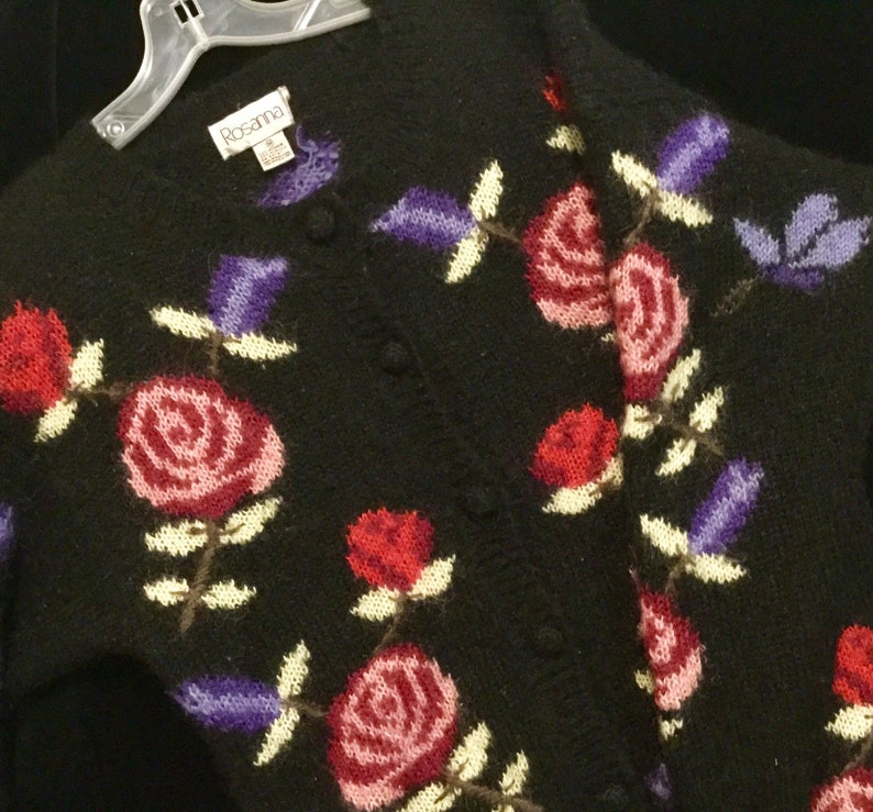 May include: Black knitted cardigan with a floral pattern featuring red, pink, and purple roses. The cardigan has a button closure and the label "Rosanna" is visible.