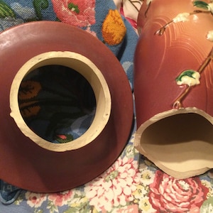 May include: A broken, vintage, brown ceramic vase with a floral design. The vase has a white interior and a white rim around the top.