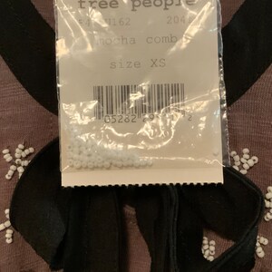 May include: A close-up of a white tag with black text that reads "free people" and "mocha comb" with a barcode and the text "size XS". The tag is attached to a brown garment with white beads and a black ribbon.