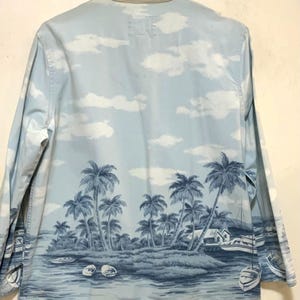May include: Light blue long-sleeve shirt with a tropical island scene. The shirt features a landscape of palm trees, boats, and a small house, all in shades of blue. The collar is a light beige color.