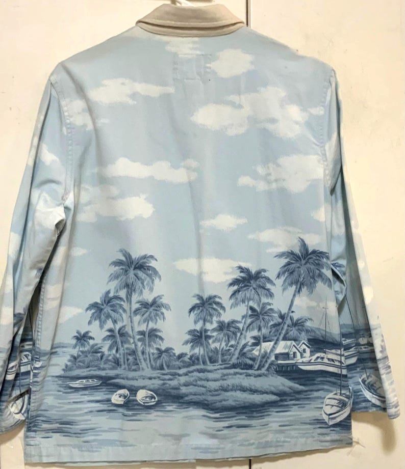 May include: Light blue long-sleeve shirt with a tropical island scene. The shirt features a landscape of palm trees, boats, and a small house, all in shades of blue. The collar is a light beige color.