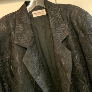 Puede incluir: Una chaqueta negra con un patrón floral en relieve. La chaqueta tiene una etiqueta que dice "Wheaton & Kidd Limited Edition".
